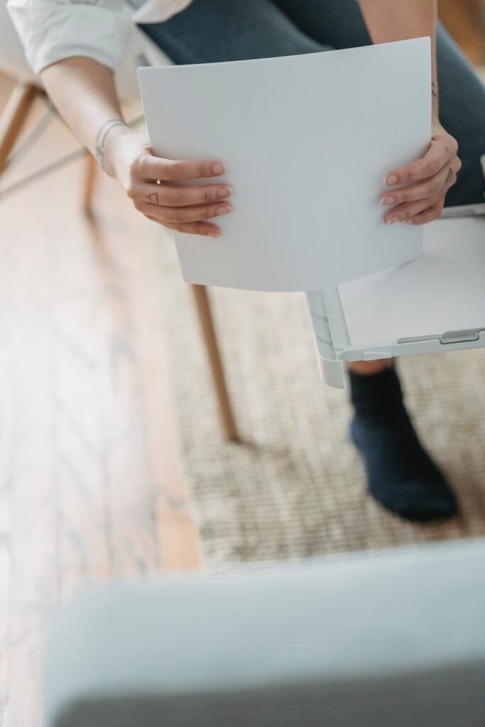 From above of crop anonymous female remote worker sitting on chair and preparing paper for printing document